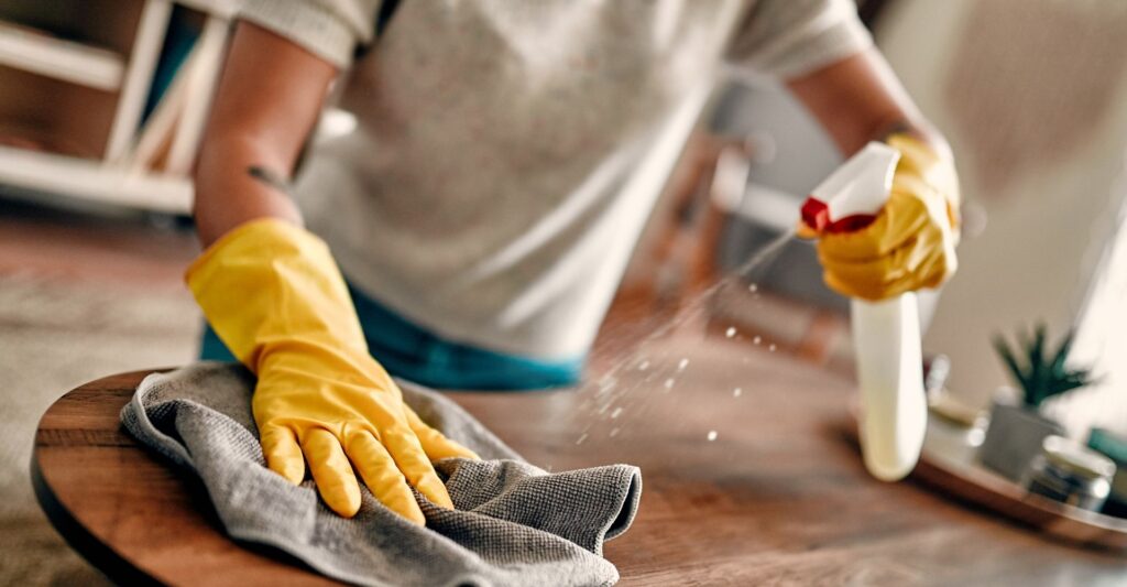 gloved hands wiping table and spraying disinfectant
