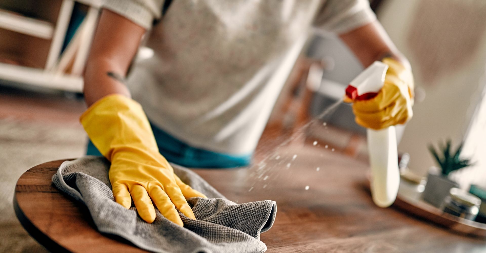 gloved hands wiping table and spraying disinfectant