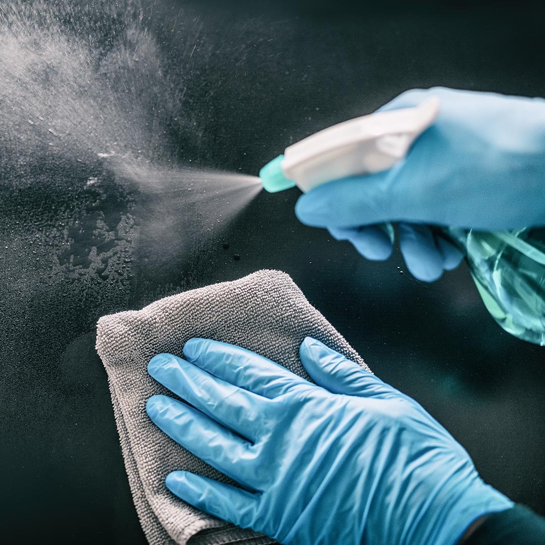Person wearing latex gloves and cleaning a surface with a spray bottle and a rag